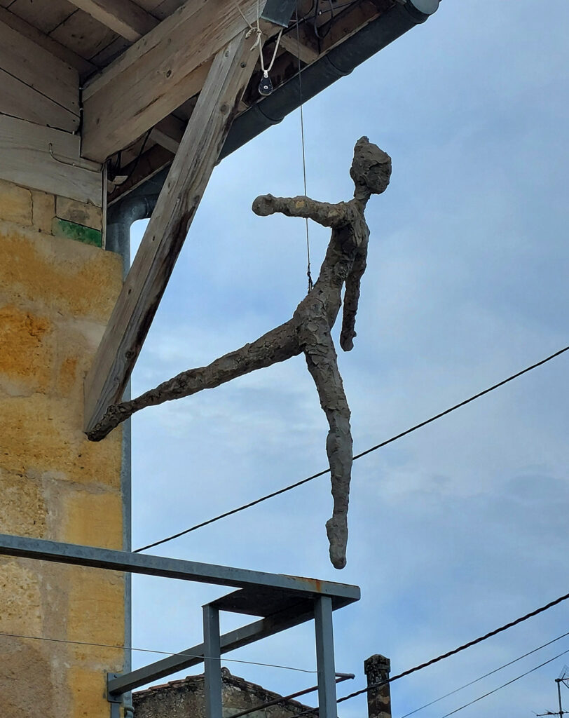 Personnage suspendu à un fil symbolisant un envol. Sculpture en béton de Philippe Doberset